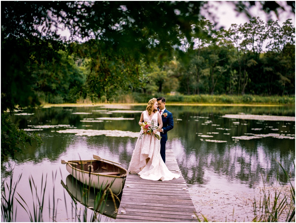 The couple poses on a dock at a lake.