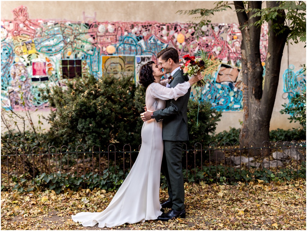 The bride and groom kiss in front of a mosaic wall