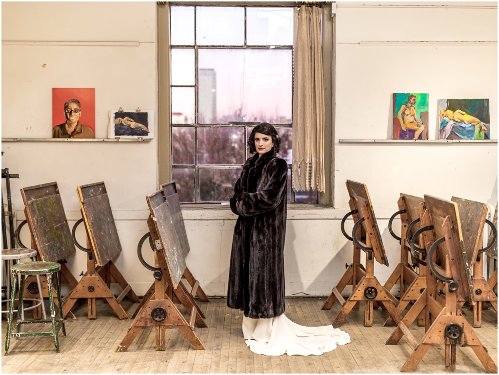 The bride wears a fur coat in an art studio.