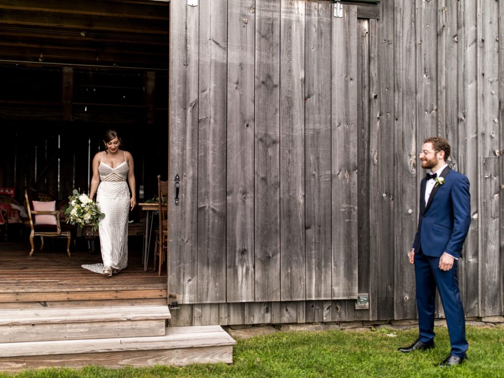 The groom stands outside the barn waiting for the bride to come out for the first look