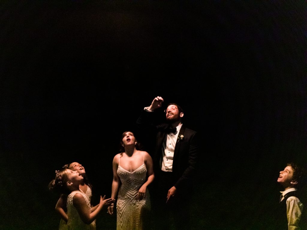 The bride, groom, and their flower girls watch a lantern float away into the night.